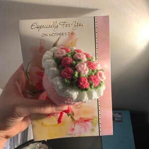 以下が含まれることがあります： ピンクと白の毛糸で編まれた花束。緑の葉っぱもついています。花束は「Especially For You On Mother's Day」と書かれたカードの上に置かれています。
