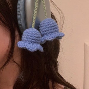 May include: A pair of blue crocheted flower charms attached to a pair of silver headphones.