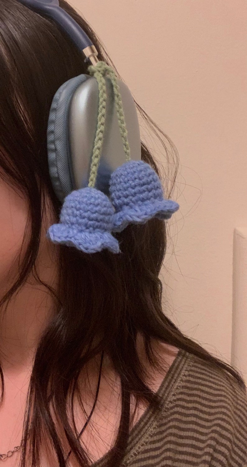 May include: A pair of blue crocheted flower charms attached to a pair of silver headphones.