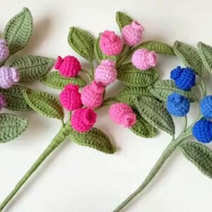 May include: Three crocheted flower stems with green leaves and purple, pink, and blue berries.