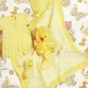 May include: A set of yellow, handmade baby items: a crocheted dress, bonnet, blanket, booties, and a plush chick. The blanket has a yellow border. The items are displayed on a patterned fabric with cartoon characters.