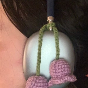May include: A pair of purple crocheted flower ear warmers with green yarn strings attached to a blue headband.