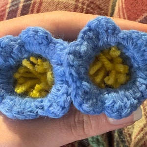 May include: Two crocheted blue flowers with yellow centers. The flowers are made with a soft yarn and have a delicate, handmade look.