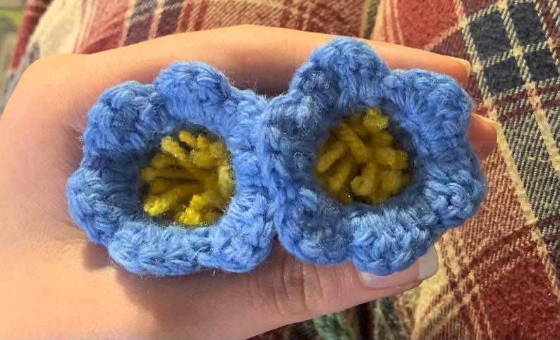May include: Two crocheted blue flowers with yellow centers. The flowers are made with a soft yarn and have a delicate, handmade look.