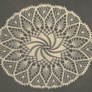 May include: Cream-colored, circular doily with an intricate lace design. The doily features a central spiral pattern surrounded by radiating, fan-like motifs. The delicate openwork creates a textured, airy appearance, perfect for home decor.