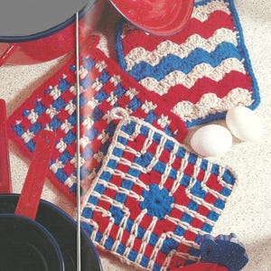 以下が含まれることがあります： 赤、白、青の手作りのかぎ針編みの鍋つかみのコレクション。鍋つかみは、波模様や中央に花がある正方形の模様など、さまざまな幾何学模様が特徴です。画像には、赤いエナメルウェアと2つの白い卵も含まれています。