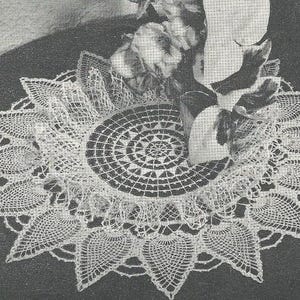 May include: A round white crocheted doily featuring a central circular grid pattern surrounded by a border of pointed, leaf-shaped motifs. The intricate needlework displays a delicate openwork design with fine thread construction throughout the piece.