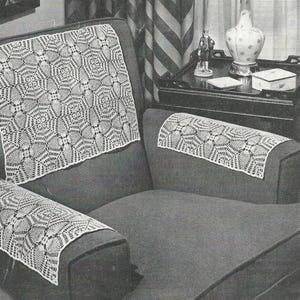May include: A close-up of a chair with white crocheted doilies on the back and armrests. The doilies have a detailed, geometric pattern. The chair is upholstered in a dark fabric, and the background includes a table with decorative items.
