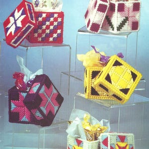 May include: Five square plastic canvas boxes with lids, featuring colorful geometric yarn patterns in red, white, purple, pink, yellow, black, and light blue. Each box contains tissue paper and small items like candies or a figurine.