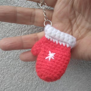 May include: Red crocheted mitten keychain with a white snowflake design and a silver chain.