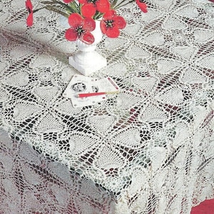 Peut inclure: Une nappe en crochet de couleur crème avec un motif répétitif en forme de cœur. Un vase blanc contenant des fleurs de coquelicot rouges est posé sur la nappe, à côté d'un petit jeu de cartes avec un stylo rouge posé dessus.
