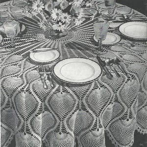 Pode incluir: Uma toalha de mesa de crochê branca suja com borda ondulada, montada para um jantar formal. A mesa é adornada com pratos brancos, talheres e copos. Um vaso de margaridas brancas está no centro.
