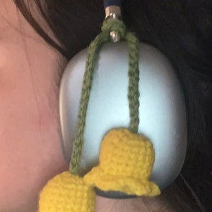 May include: A pair of yellow crocheted bells hanging from a blue and green cord attached to a silver object. The bells are attached to a silver object with a blue handle.