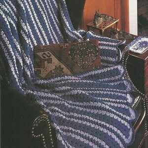 May include: A blue and white striped crochet blanket draped over a dark leather armchair. A decorative pillow with a geometric pattern rests on the blanket. The blanket has a scalloped edge.
