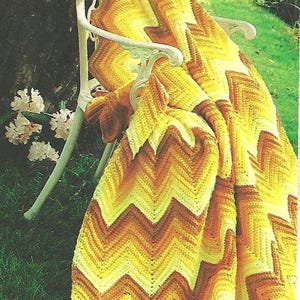 May include: A yellow, orange, and white crocheted blanket with a chevron pattern draped over a white metal chair in a garden setting.