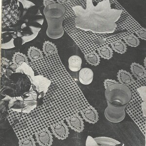 May include: A set of white rectangular crochet placemats featuring a grid pattern and decorative scalloped edges. The placemats are arranged with clear drinking glasses, a leaf-shaped dish, a silver fork, and two small white salt and pepper shakers.