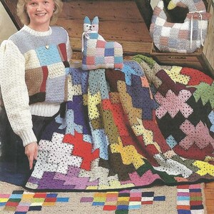 May include: A collection of crocheted items including a patchwork sweater with cream sleeves, a cat-shaped pillow, a goose-shaped pillow, a large multi-colored granny square blanket, and a rectangular rug with a colorful checkered border.