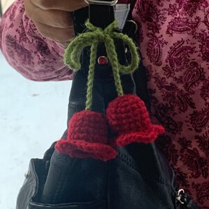 May include: A black leather handbag with a green and red crocheted cherry charm attached to the handle.