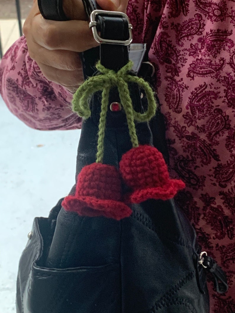May include: A black leather handbag with a green and red crocheted cherry charm attached to the handle.