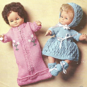 May include: Two dolls with molded facial features. One doll has brown hair and wears a long-sleeved pink knitted sleeper with a front zipper and white floral embroidery. The second doll has blonde hair and wears a blue knitted dress, bonnet, and booties.