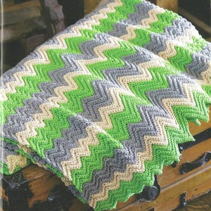 May include: A crocheted chevron blanket in shades of green, gray, and beige. The blanket is folded and draped over a wooden chest.
