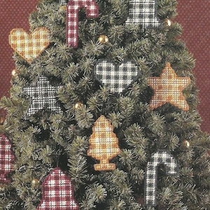 May include: A green artificial Christmas tree decorated with various plaid fabric ornaments including stars, candy canes, hearts, bells, and trees in red, yellow, black, and white. A small gift box wrapped in red patterned paper sits at the base.