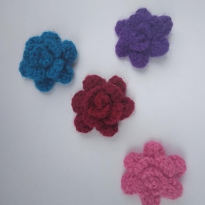Può includere: Quattro fiori all'uncinetto in diversi colori: blu, viola, rosa e bordeaux.