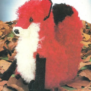 May include: A plush fox toy crafted with fuzzy red, white, and black yarn. The fox features a bright red head and back, a white chest and muzzle, black ears, and black legs. It has small dark eyes and a black nose, with a textured, soft appearance.