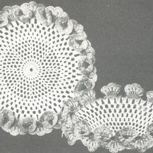 Puede incluir: Dos tapetes blancos de ganchillo. Uno es circular con un borde festoneado, y el otro tiene forma de semicírculo con un borde festoneado similar. El diseño calado es visible en ambas piezas.