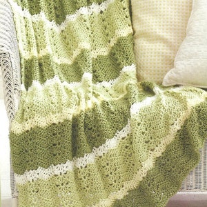 May include: A crocheted throw blanket in shades of green and white with a scalloped edge. The blanket is draped over a white wicker chair with two pillows.