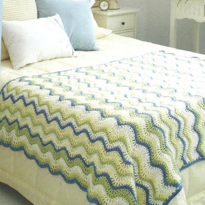 May include: A white bed with a blue, green, and white crocheted throw blanket. The blanket has a chevron pattern. The bed has a white headboard and a white nightstand with a lamp.