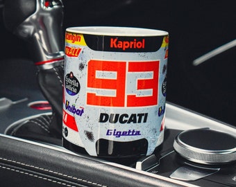 May include: A white ceramic mug with a red and black racing design. The mug features the number "99" in red, the word "DUCATI" in black, and the word "Gigetta" in black. The mug also has the word "Kapriol" in black at the top.