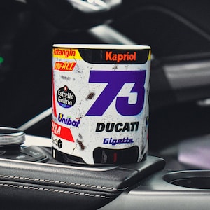May include: White ceramic mug with a distressed, vintage racing design. The mug features a large purple number "73" with the word "DUCATI" and the sponsor logos "Kapriol", "Estrella Galicia", "Unibat", and "Gigetta".