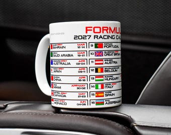 May include: A white ceramic mug featuring the Formula 1 2027 Racing Calendar printed in black and red text. The design includes a list of sixteen race locations, corresponding national flags, and specific dates for each event in a two-column layout.
