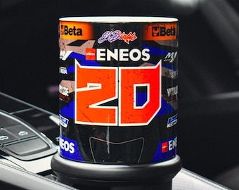 以下が含まれることがあります： オレンジと白で「ENEOS 20」と書かれた黒と青のトラベルマグ。マグは車のカップホルダーに入っています。