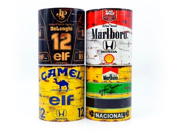 May include: Four yellow and black ceramic mugs with vintage racing car sponsor logos. The mugs feature logos for John Player Special, Marlboro, Camel, and Elf. The mugs have a distressed, weathered look.
