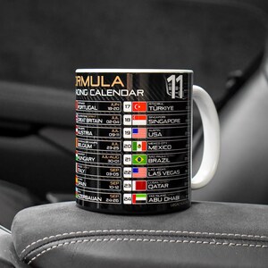 May include: A black ceramic mug featuring a Formula 1 racing calendar with a carbon fiber pattern background. The design includes a list of race locations, dates, and national flags, with the text Formula Racing Calendar and the number 11 printed.