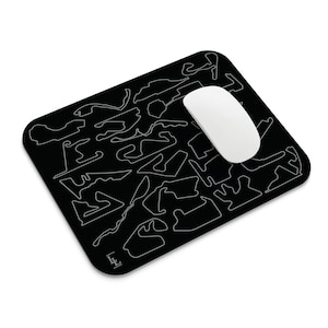 May include: Black rectangular mousepad featuring a white outline design of various race tracks. A white wireless mouse rests on the pad. The mousepad has a rounded corner design. The lower left corner has the initials "LE".
