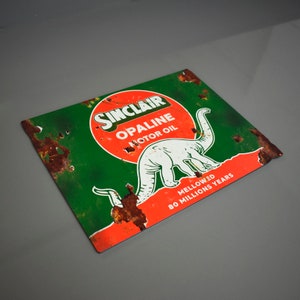 May include: A vintage Sinclair Opaline Motor Oil sign with a green background, red circle, and a white dinosaur. The sign has rust and is faded. The text on the sign reads "Sinclair Opaline Motor Oil Mellowed 80 Millions Years".