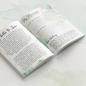 May include: An open journal with a green and white watercolor design on the cover. The text on the page reads "Say hello to June" and "My Monthly Reflections". The journal is a tool for self-reflection and goal setting.