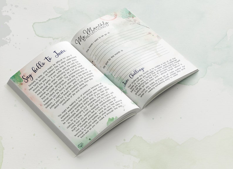 May include: An open journal with a green and white watercolor design on the cover. The text on the page reads "Say hello to June" and "My Monthly Reflections". The journal is a tool for self-reflection and goal setting.