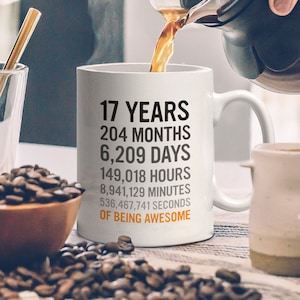 May include: White ceramic coffee mug with black text that reads "17 Years, 204 Months, 6,209 Days, 149,018 Hours, 8,941,129 Minutes, 536,467,741 Seconds of Being Awesome".