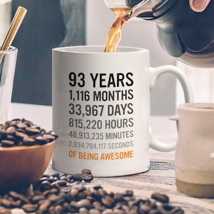 May include: White ceramic coffee mug with black text that reads "93 Years, 1,116 Months, 33,967 Days, 815,220 Hours, 48,913,235 Minutes, 2,934,794,117 Seconds of Being Awesome".