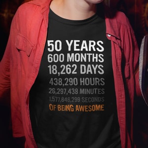 May include: A black t-shirt with white text that reads "50 Years 600 Months 18,262 Days 438,290 Hours 26,297,438 Minutes 1,577,846,299 Seconds of Being Awesome".