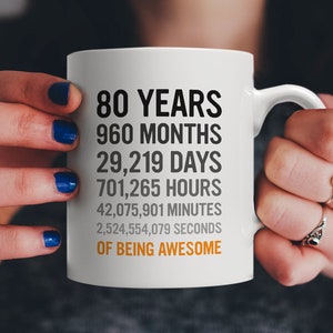Puede incluir: Taza de cerámica blanca con texto negro que dice "80 años 960 meses 29.219 días 701.265 horas 42.075.901 minutos 2.524.554.079 segundos de ser increíble".