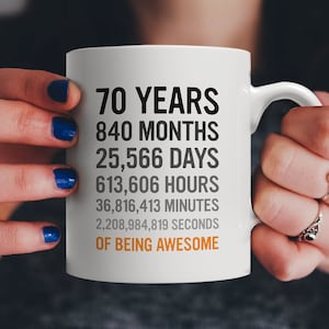 May include: White ceramic mug with black text that reads "70 Years, 840 Months, 25,566 Days, 613,606 Hours, 36,816,413 Minutes, 2,208,984,819 Seconds of Being Awesome".