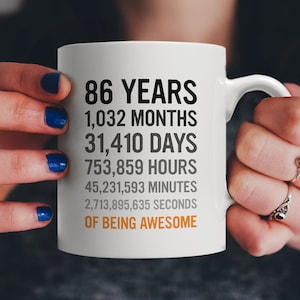 May include: White ceramic mug with black text that reads "86 Years, 1,032 Months, 31,410 Days, 753,859 Hours, 45,231,593 Minutes, 2,713,895,635 Seconds of Being Awesome".