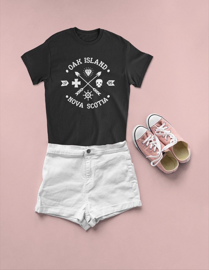 May include: Black t-shirt with a white graphic design that says "Oak Island, Nova Scotia" with a diamond, skull, cross, and compass design. White denim shorts and pink sneakers.