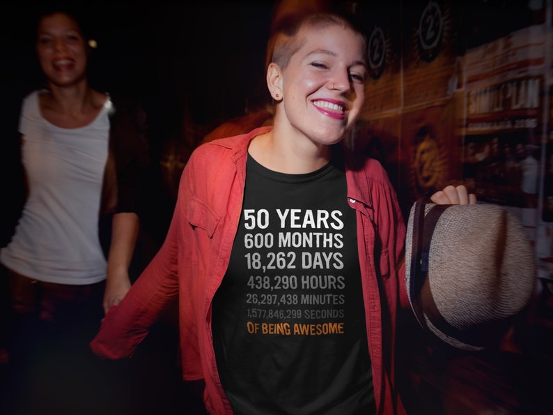 May include: A black t-shirt with white text that reads "50 Years 600 Months 18,262 Days 438,290 Hours 26,297,438 Minutes 1,577,846,299 Seconds of Being Awesome".