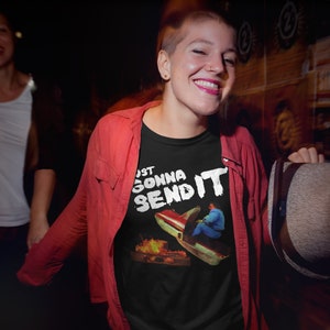 K&ouml;nnte beinhalten: Ein schwarzes T-Shirt mit einem wei&szlig;en Aufdruck einer Person, die ein Auto von einer Rampe mit Flammen f&auml;hrt, und dem Text "Just Gonna Send It".